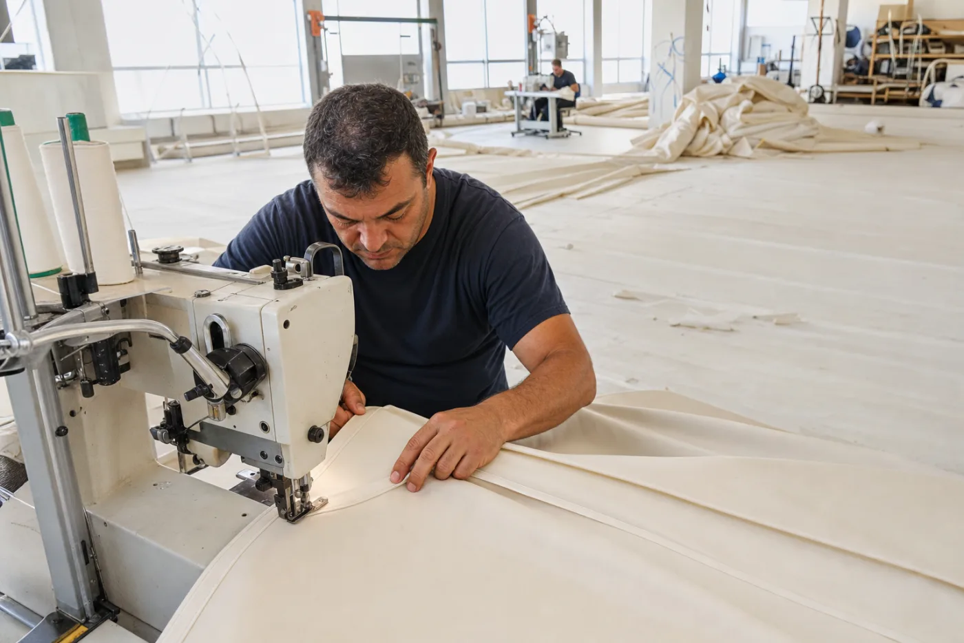 A canvas worker sewing a large panel on a sail loft floor